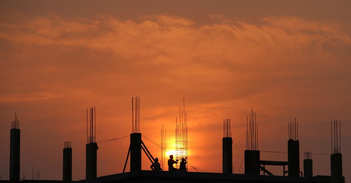 Silhouette of workers on a construction site against a vibrant sunset sky.